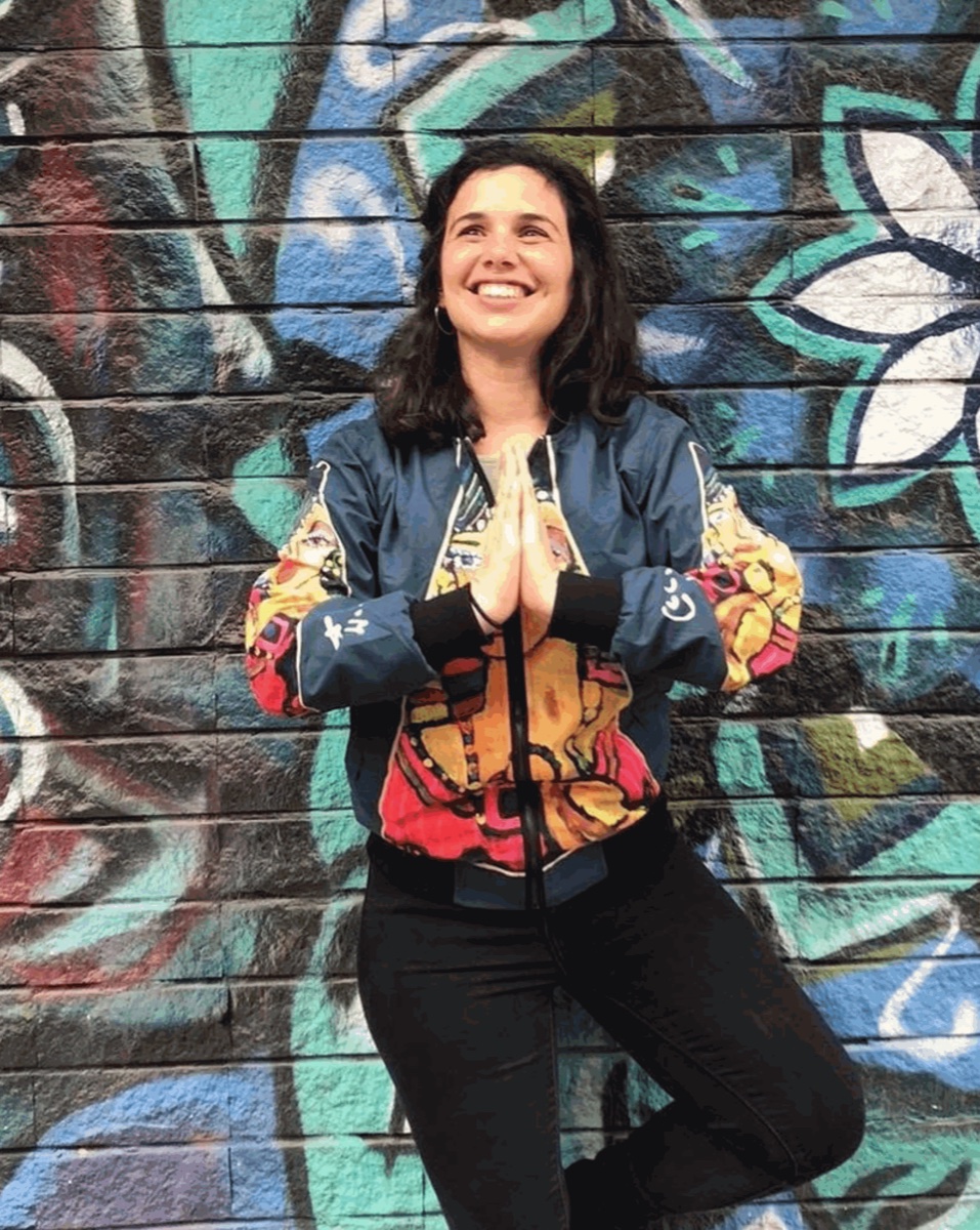 Reut smiling in a colorful jacket in front of a graffiti wall